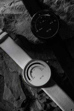 Black and white image of two minimalist wristwatches on a textured rock surface.