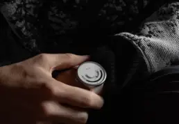 A person wearing a black and white patterned sweater holds a modern, minimalist wristwatch with a unique circular display.